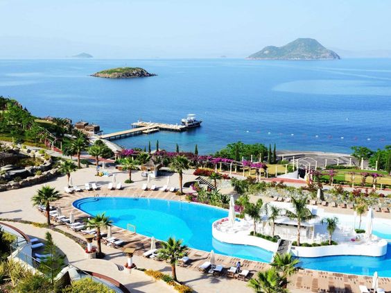 Ancient ruins at a historic Mediterranean port visited by a cruise, surrounded by lush landscapes.